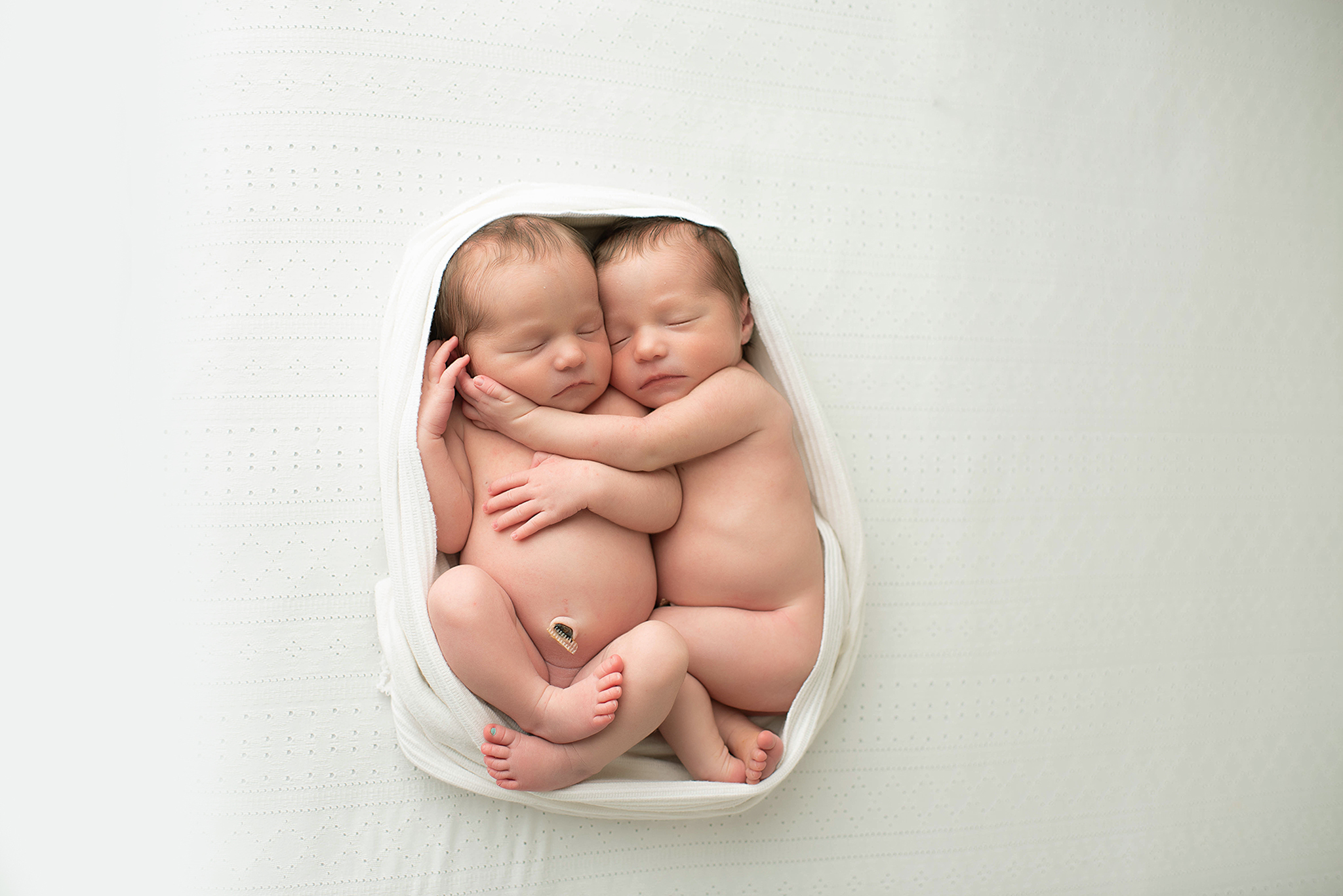 Newborn baby twins cuddle in a white blanket on a bed childbirth classes jacksonville fl