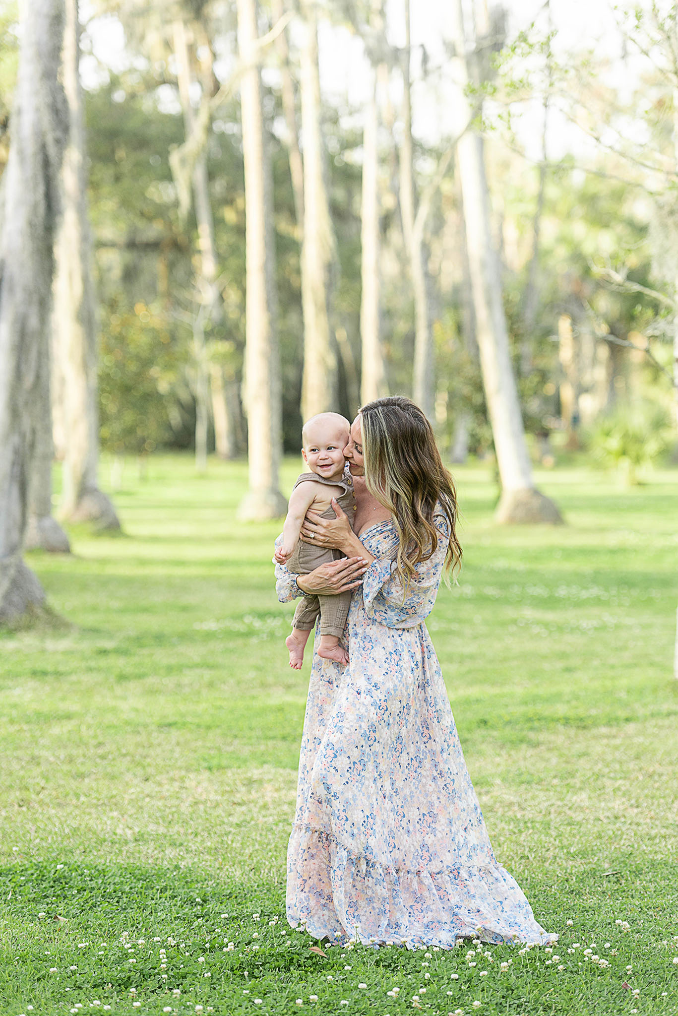 A mother walks through a park in a long floral dress with her toddler son
