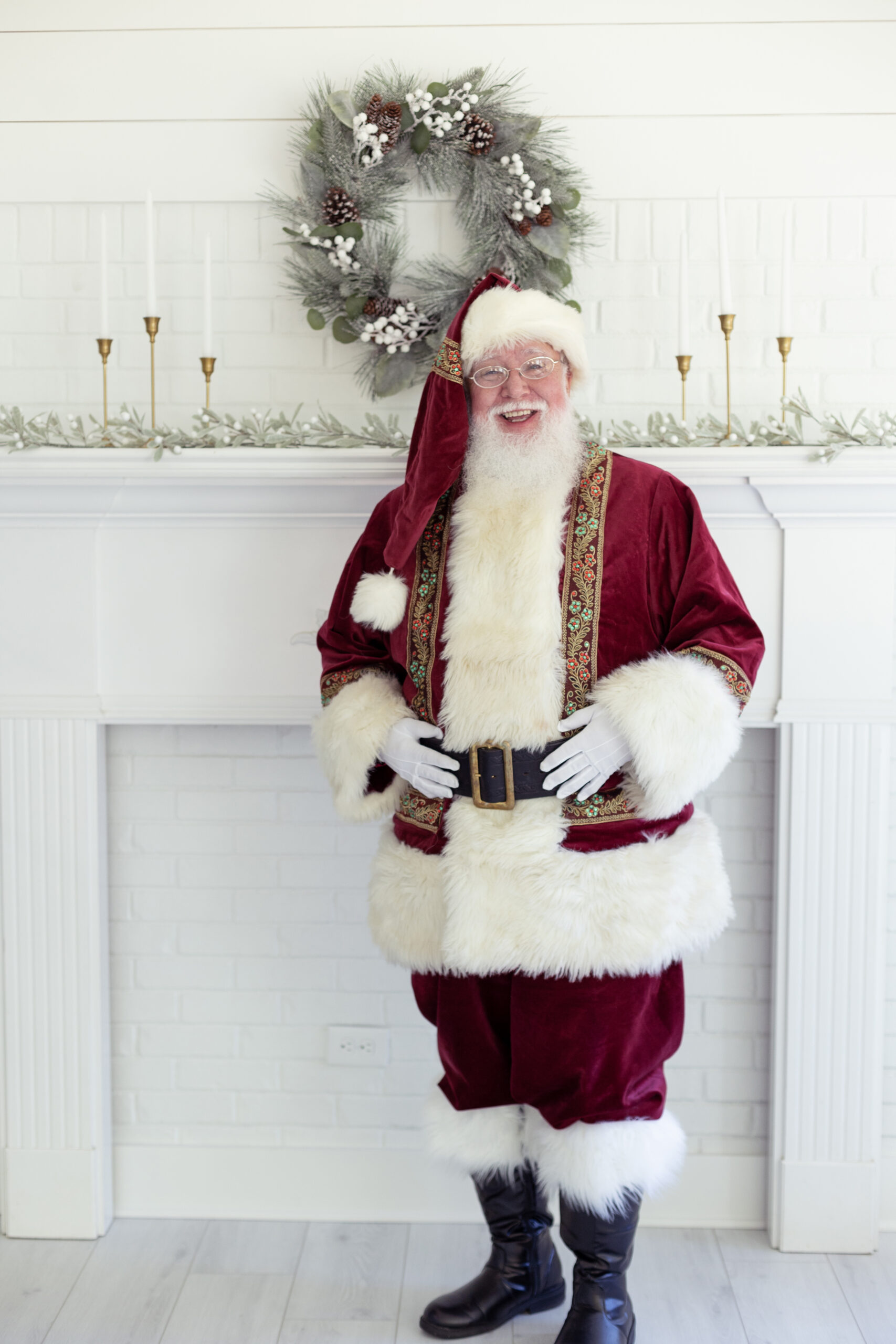 santa standing in his red suit by a white fireplace