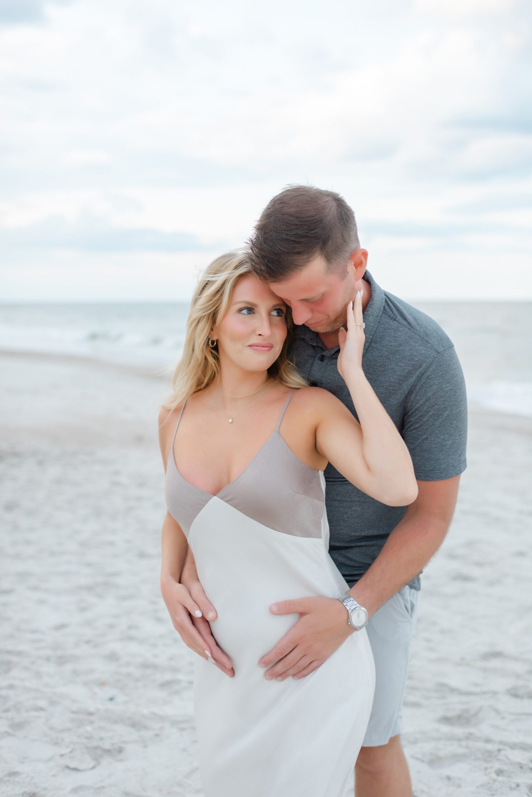 A happy expecting couple snuggles while holding the bump on a beach after some prenatal yoga jacksonville