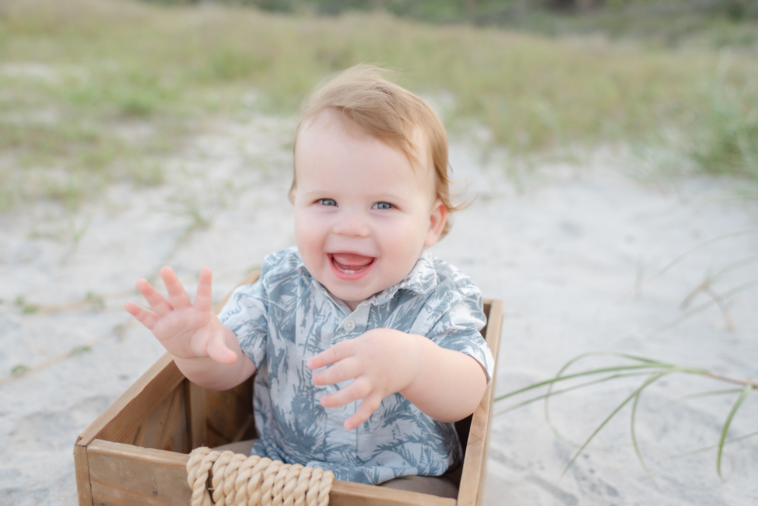 A happy toddler in a button down shirt plays in a wooden box on a beach Children's Clothing Stores Jacksonville FL