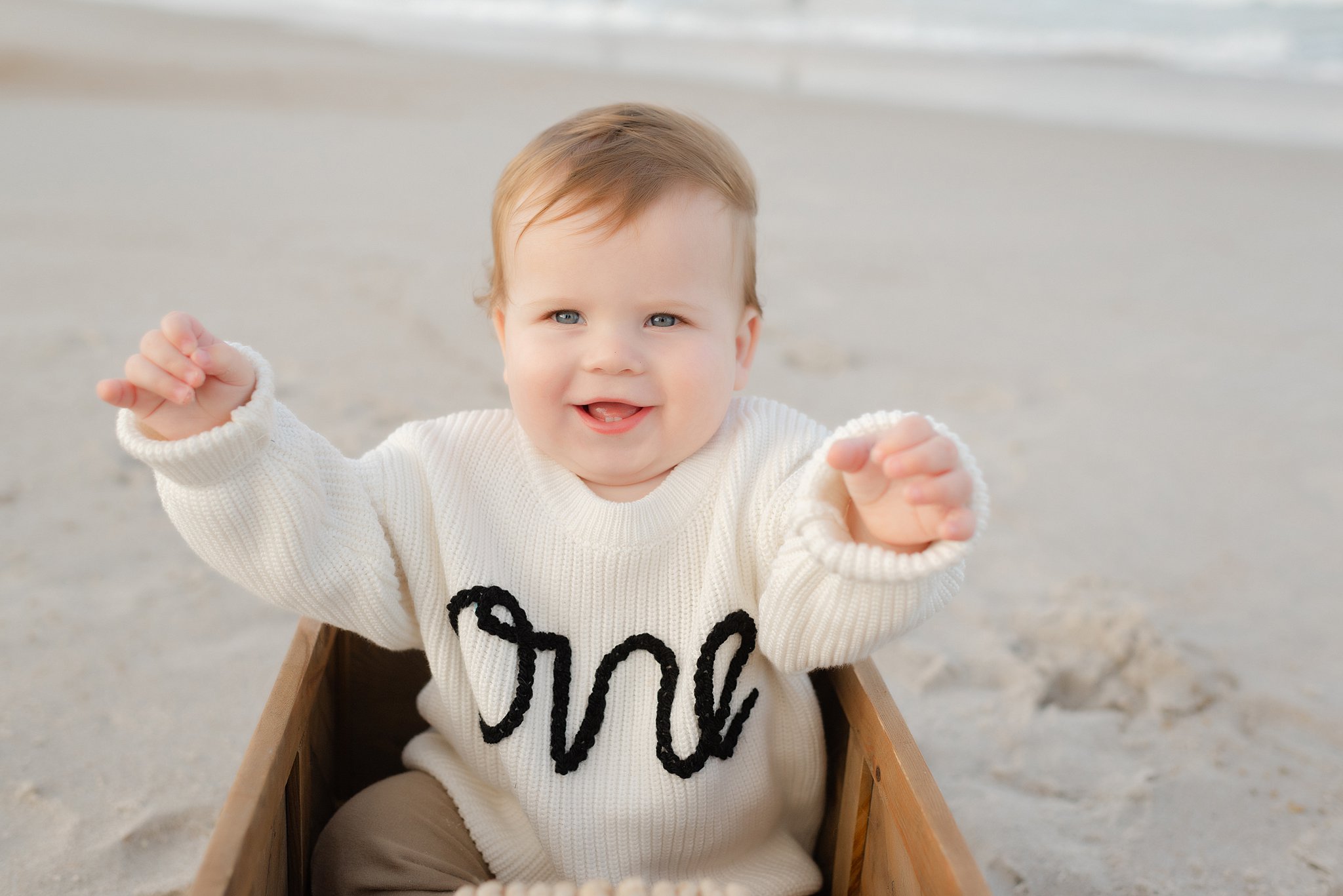 A happy toddler sits in a wooden wagon on a beach with arms out after some parenting classes jacksonville fl