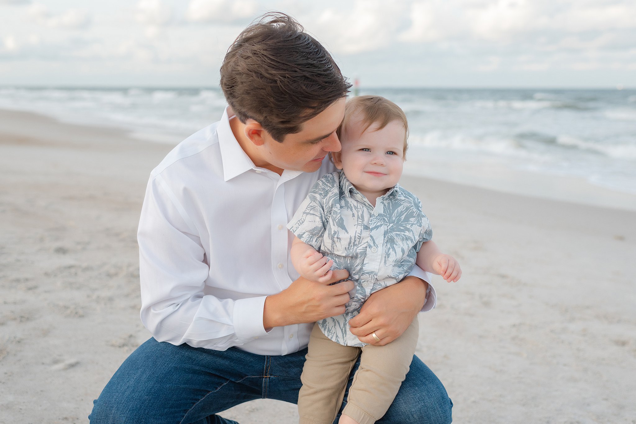 A happy dad plays with his toddler son on his knee on a beach thanks to parenting classes jacksonville fl