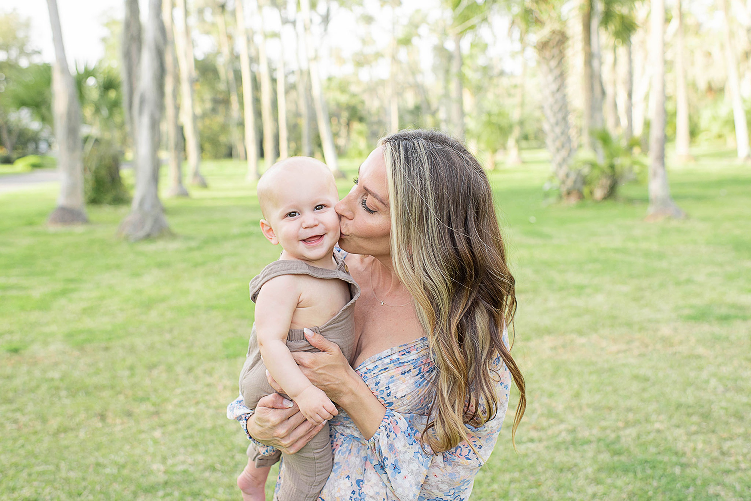 A happy mom kisses the cheek of her infant son in her arms while standing in a park after some pelvic floor therapy jacksonville fl