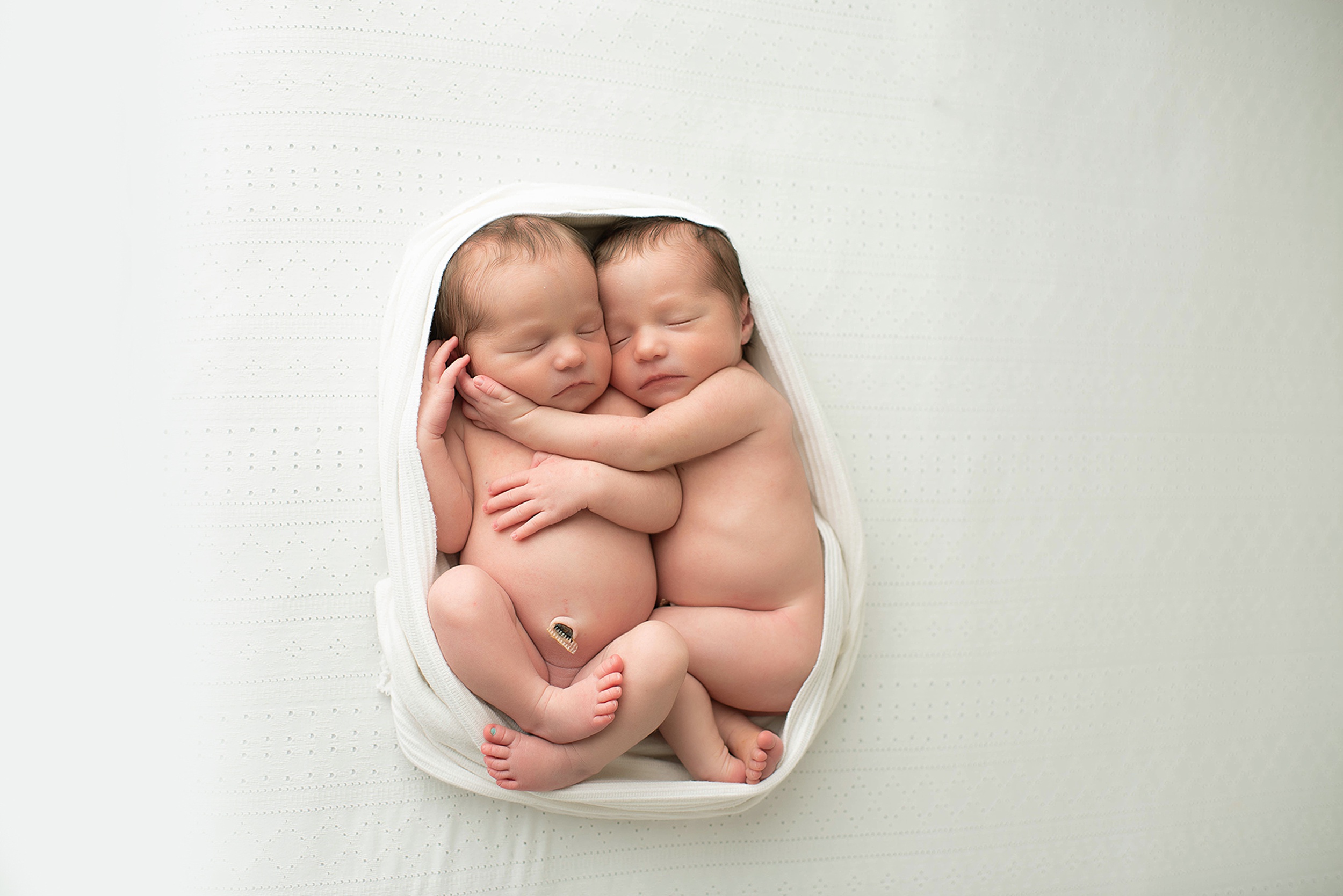 Newborn baby twin sisters cuddle while wrapped together in a swaddle after mom got placenta encapsulation jacksonville fl