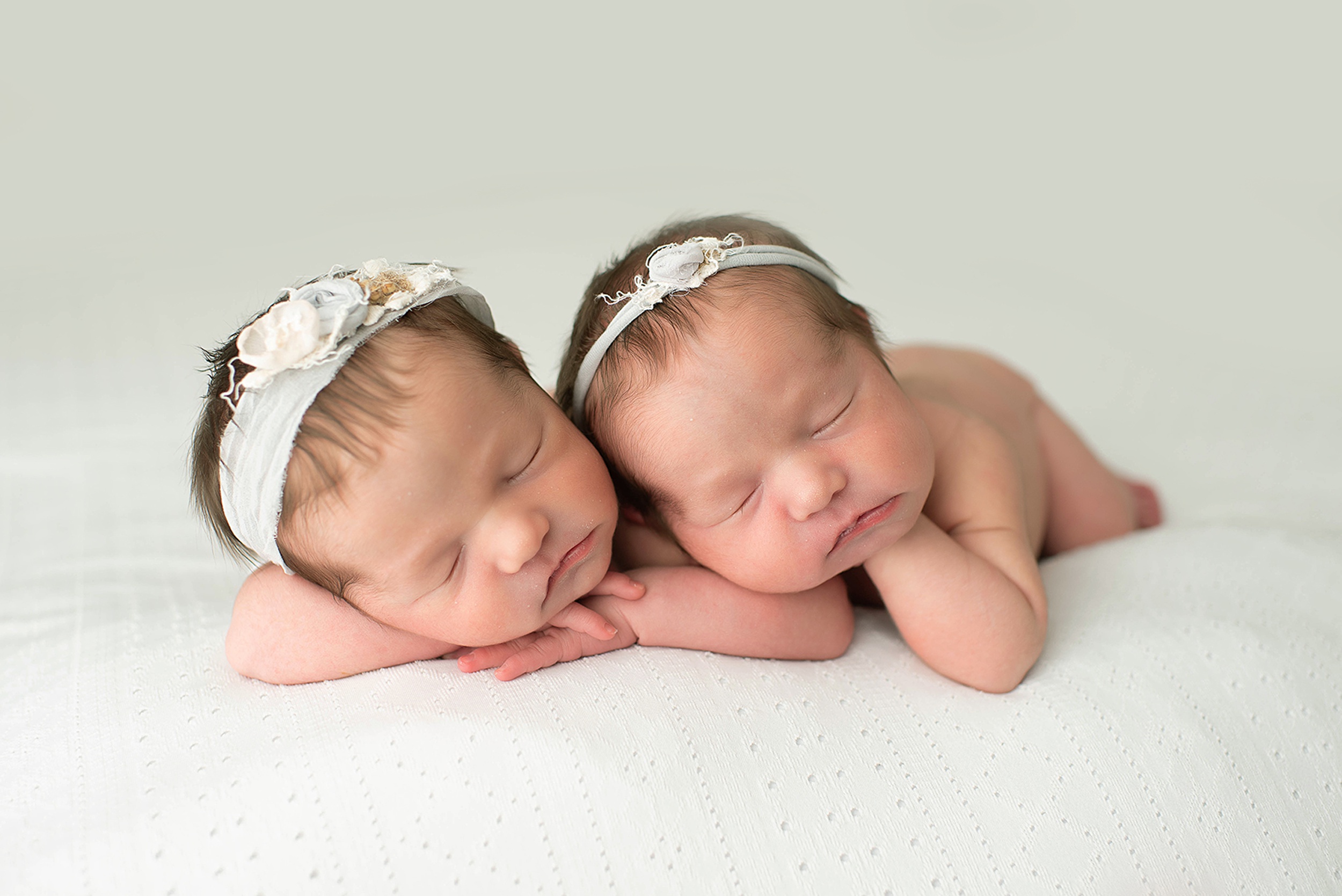 Newborn baby twins sleep on top of each other on a white bed in a studio before some placenta encapsulation jacksonville fl