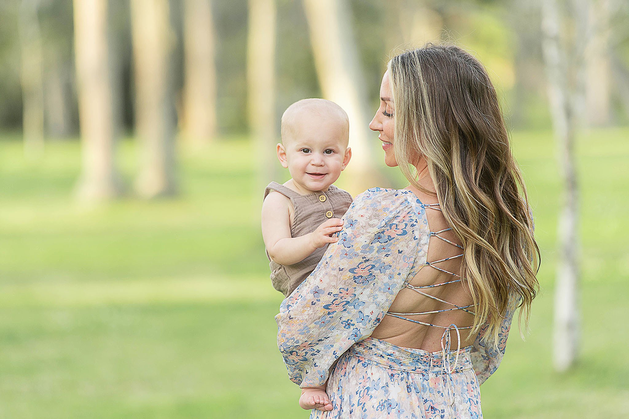 An infant baby smiles big while sitting in mom's arms in a park at sunset after some Mommy And Me Classes Jacksonville FL