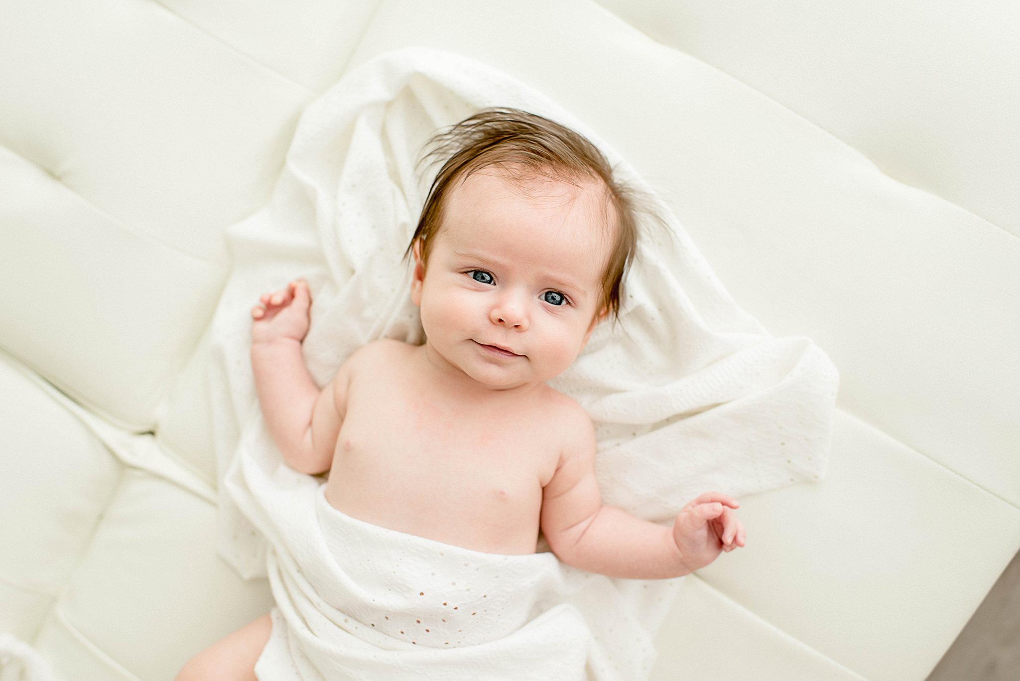 An infant baby lays on a bed with eyes open under a white blanket before visiting fall festivals jacksonville fl