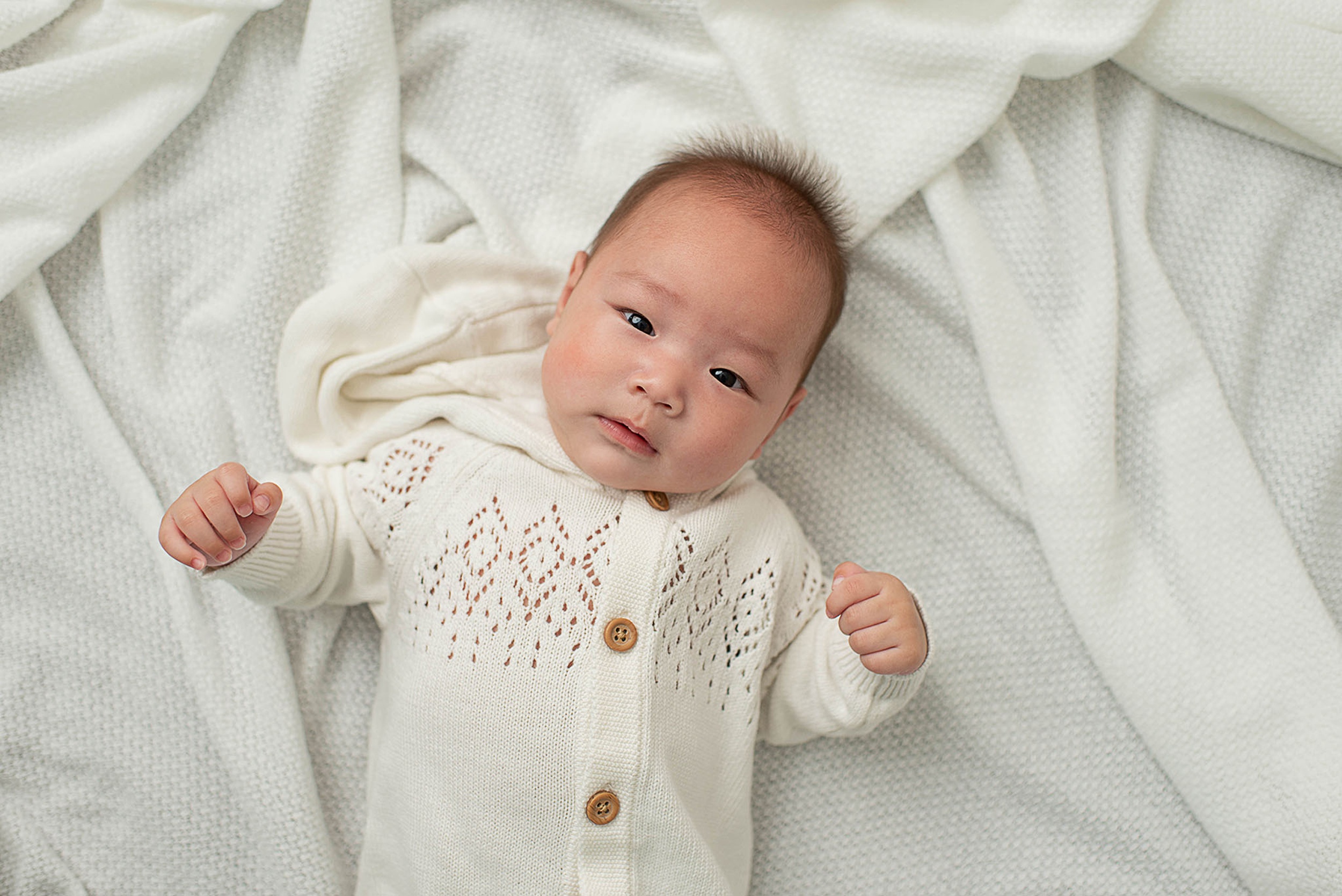 A newborn baby lays on a bed of blankets in a white knit onesie with eyes open after visiting toy stores jacksonville