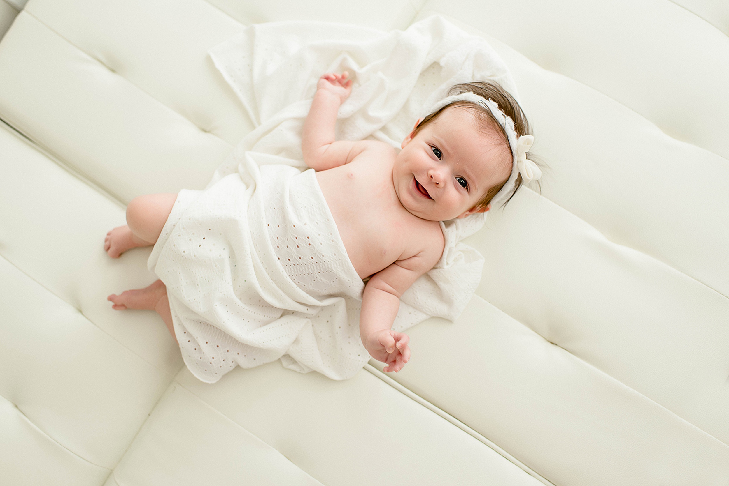 A giggling infant girl wrapped in a white blanket on a leather couch before visiting toy stores jacksonville