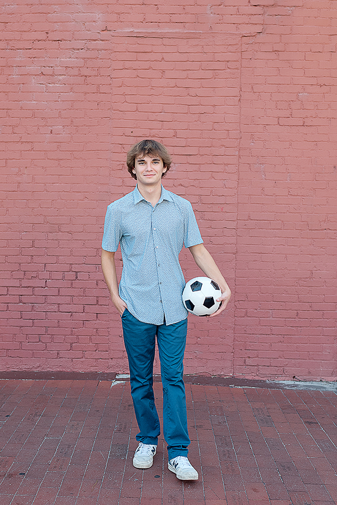 boy standing in front of red wall holding a soccer ball