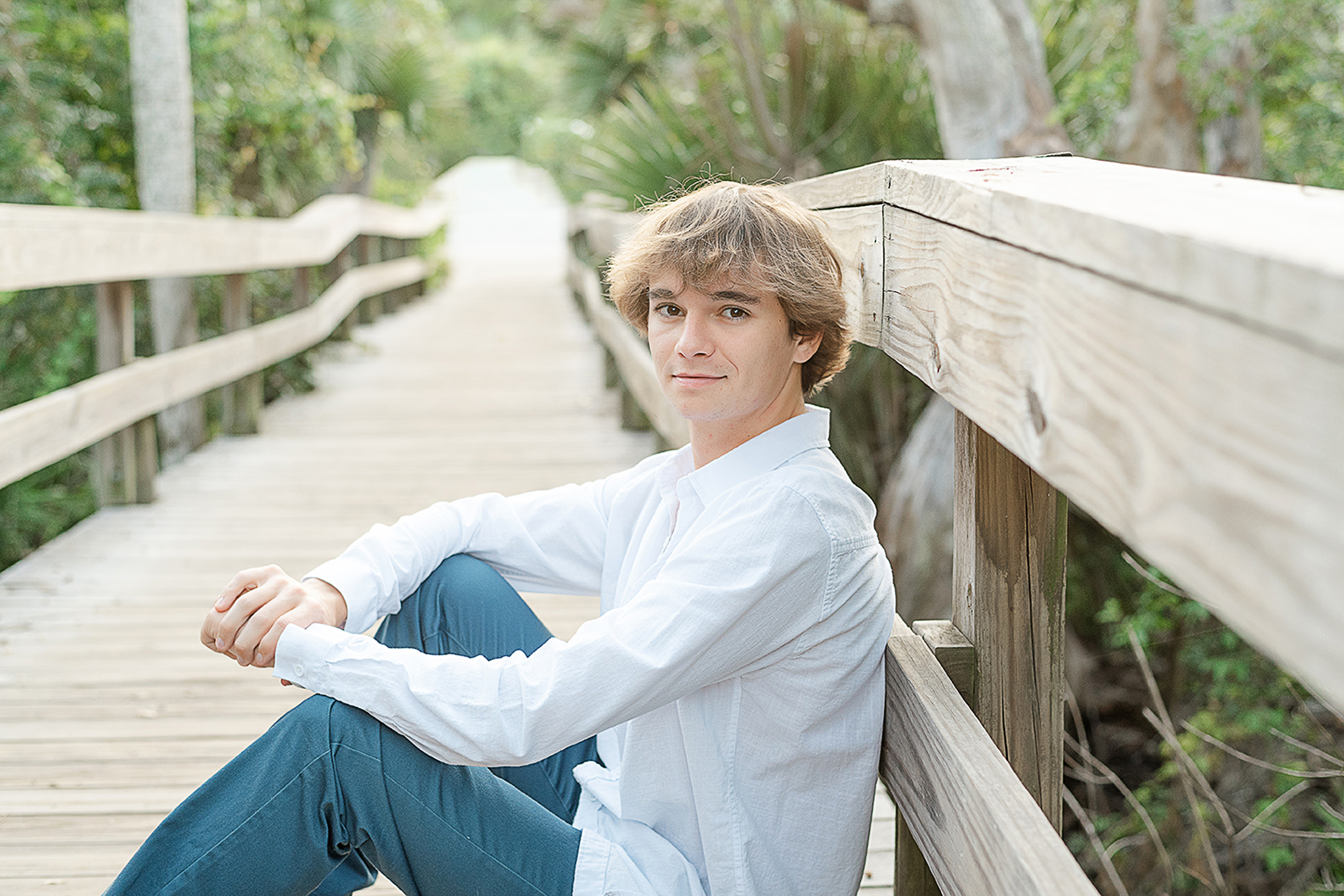 boy sitting pier at the beach in blue pants white shirt