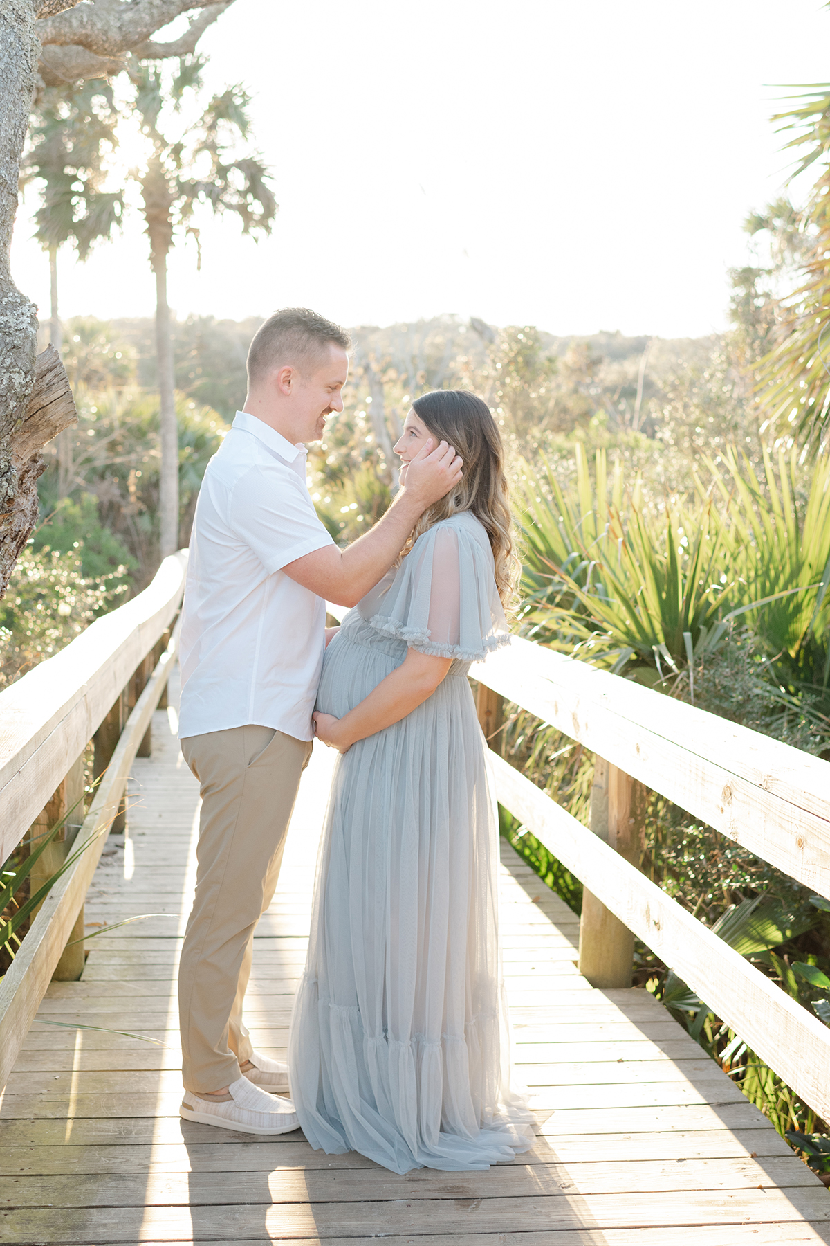 dad to be holding moms face sweetly and mom to be is holding her pregnant belly