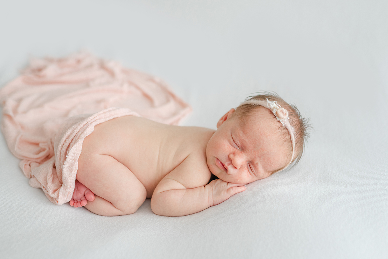 Newborn baby girl wrapped in blush on cream blanket in Jacksonville FL studio