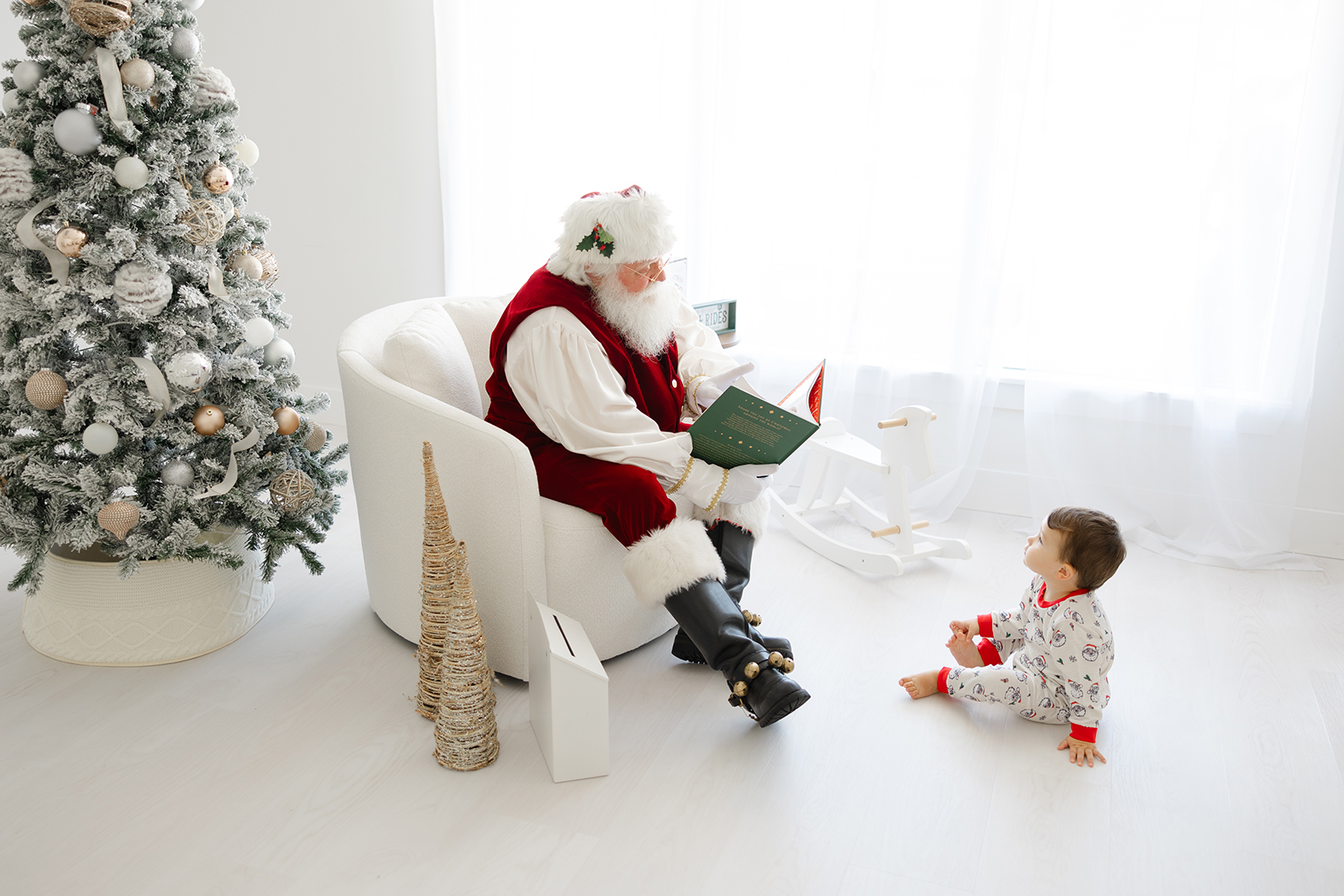 little boy sitting on white floor listening to santa read a christmas book while sitting on a white chair