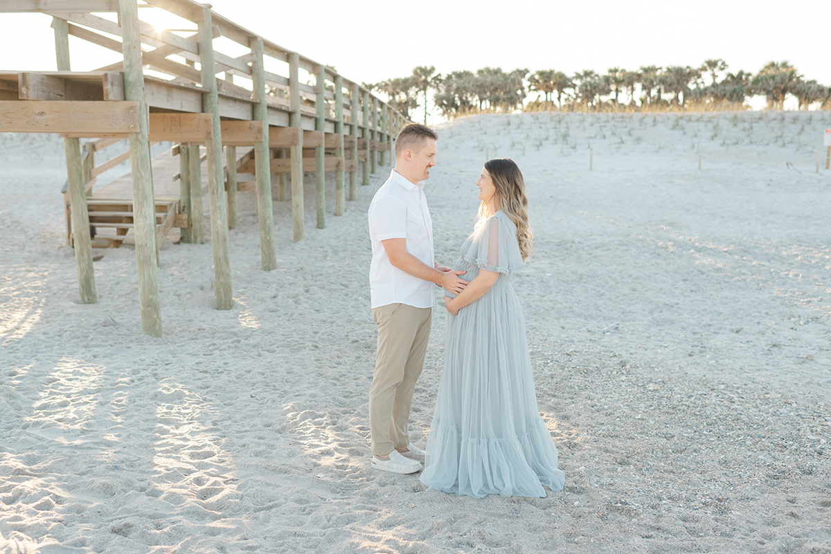 dad to be is standing with mom to be at the beach