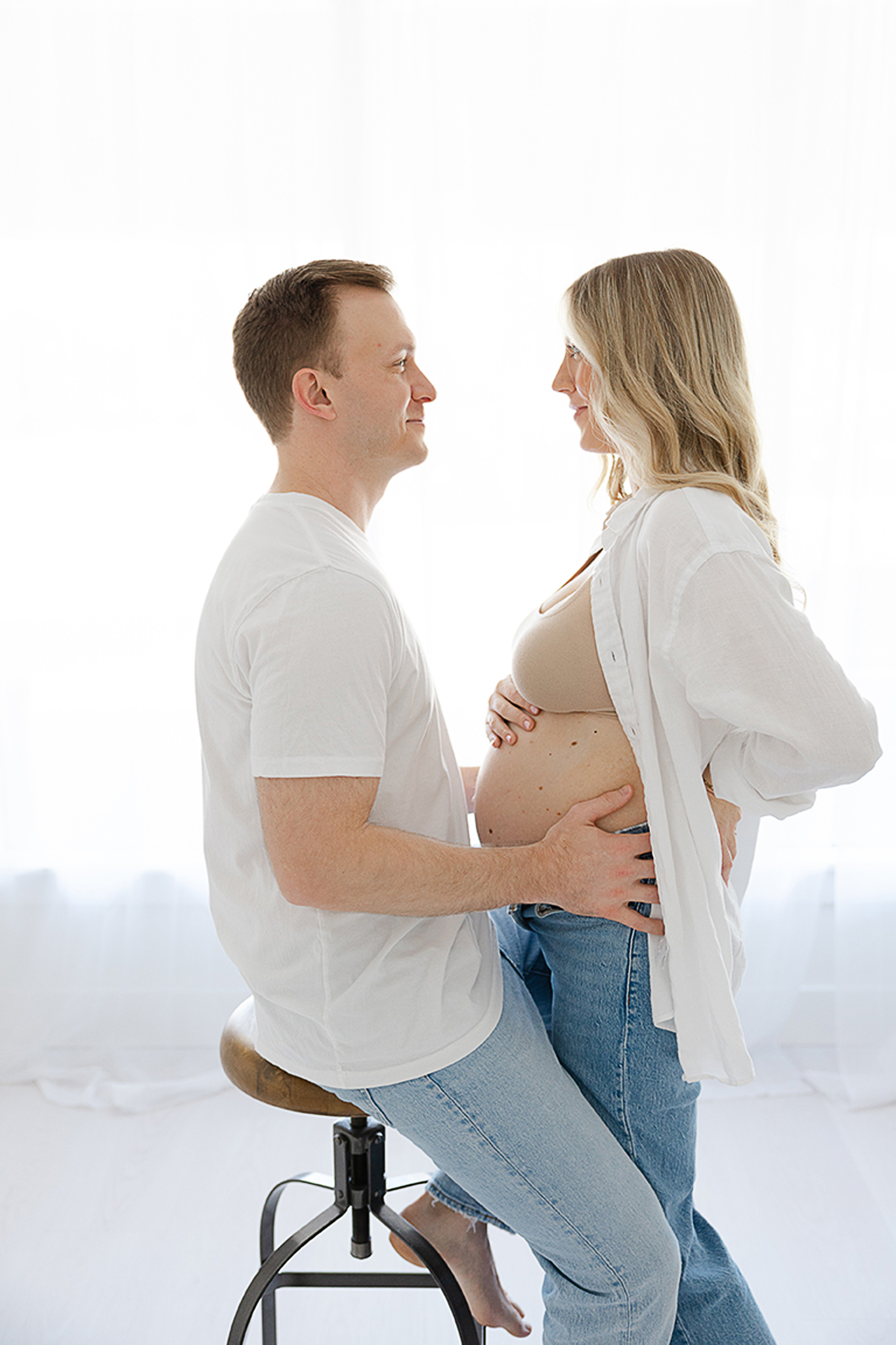 mom with her baby bump exposed while she wears white button down shirt and jeans