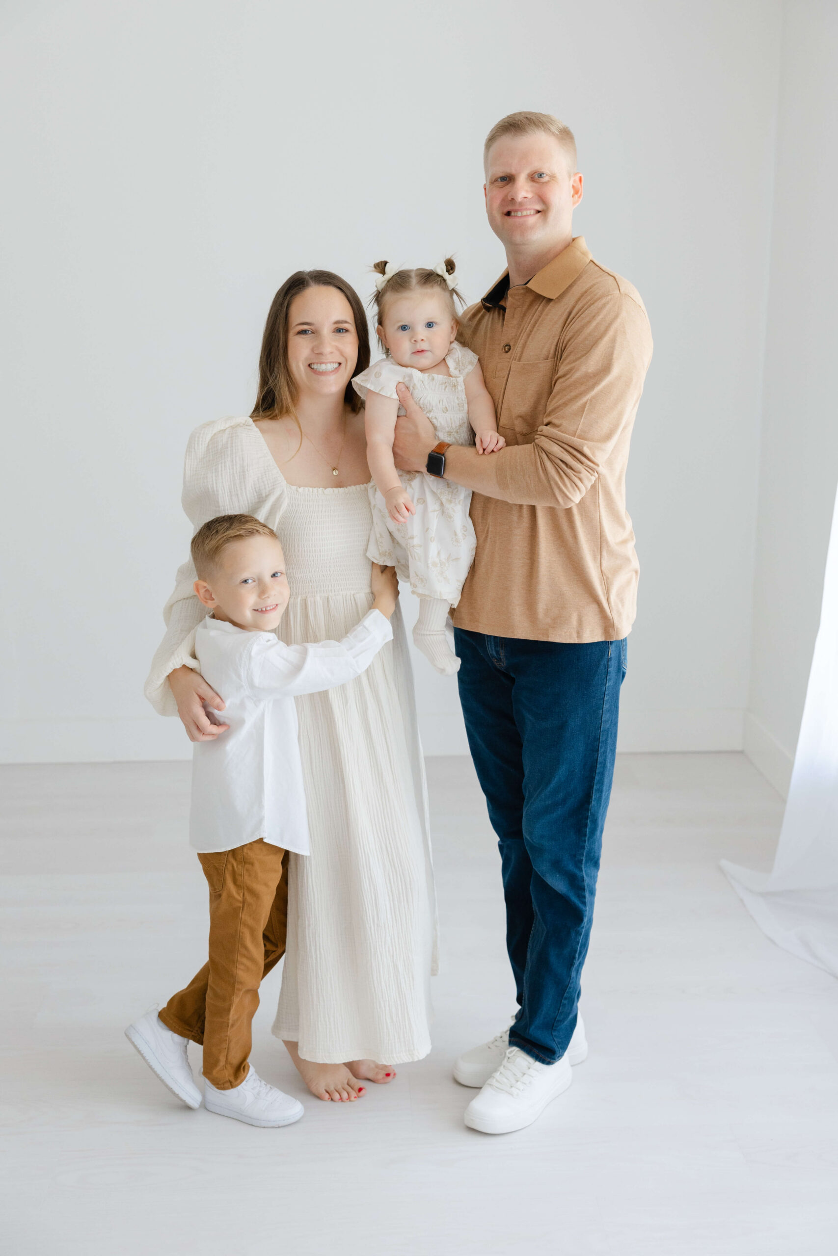 A smiling mom and and dad stand in a studio hugging and holding their toddler son and younger daughter after visiting children's museums in Jacksonville, FL