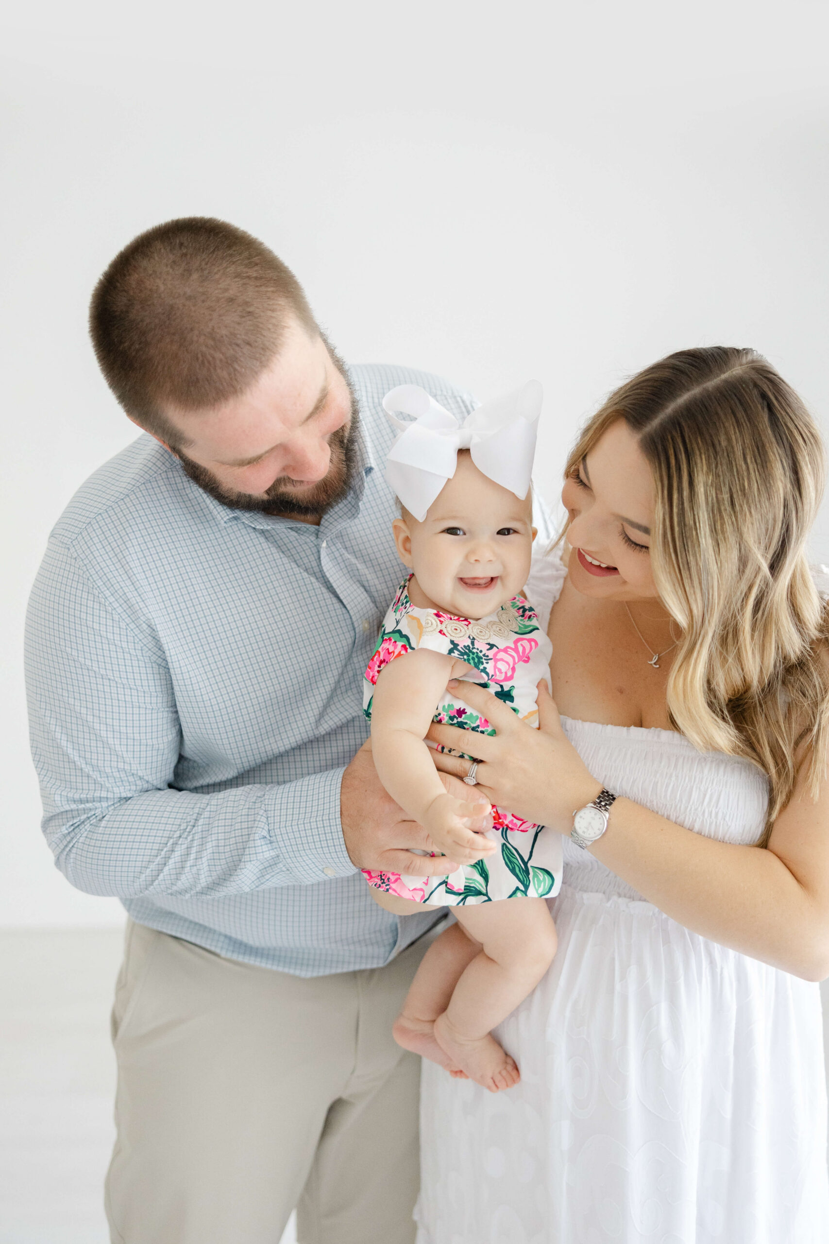 Happy mom and dad play with their toddler daughter in a bright spring onesie in a studio after finding an au pair in jacksonville fl
