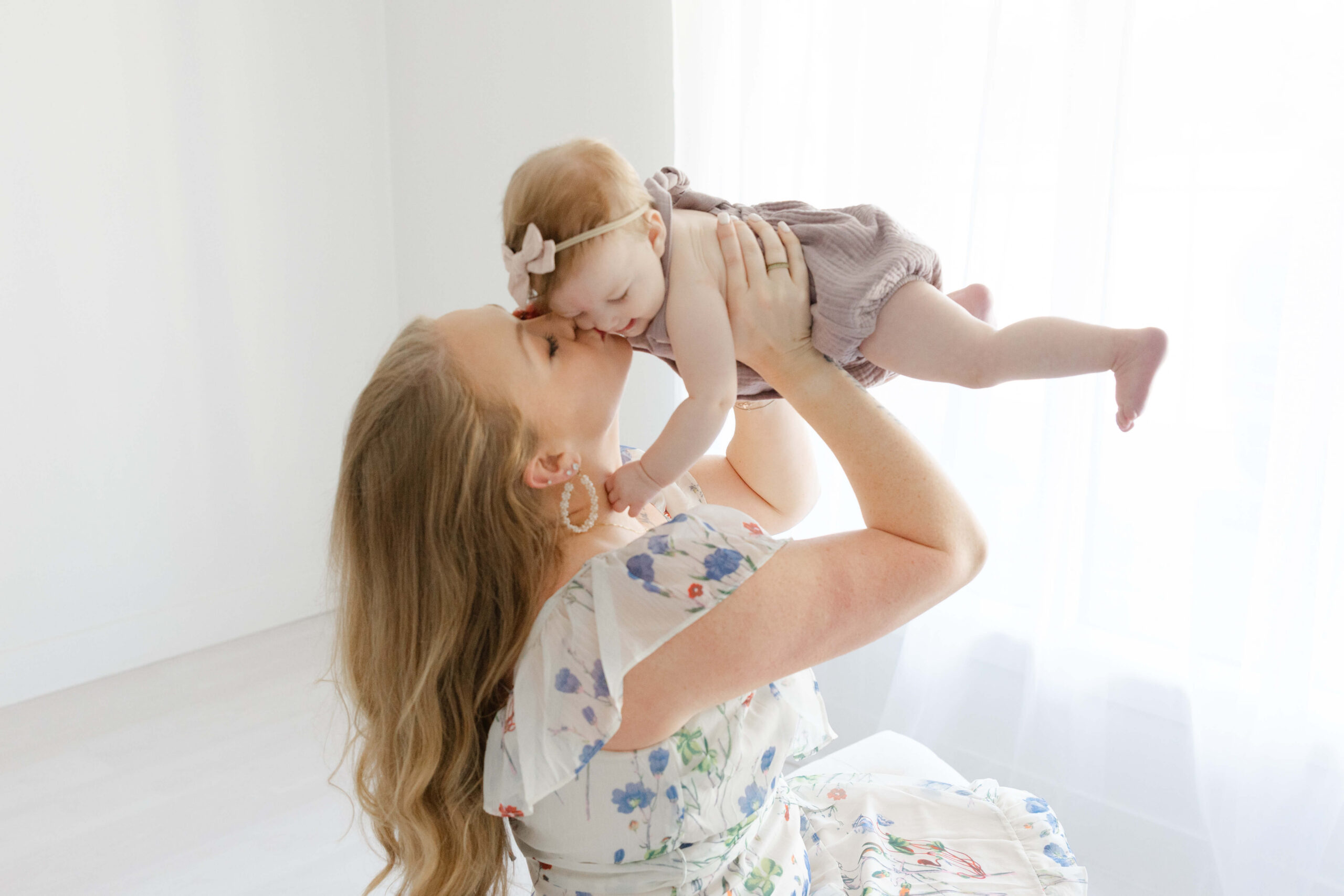A happy mom lifts her toddler daughter while sitting in a window in a studio