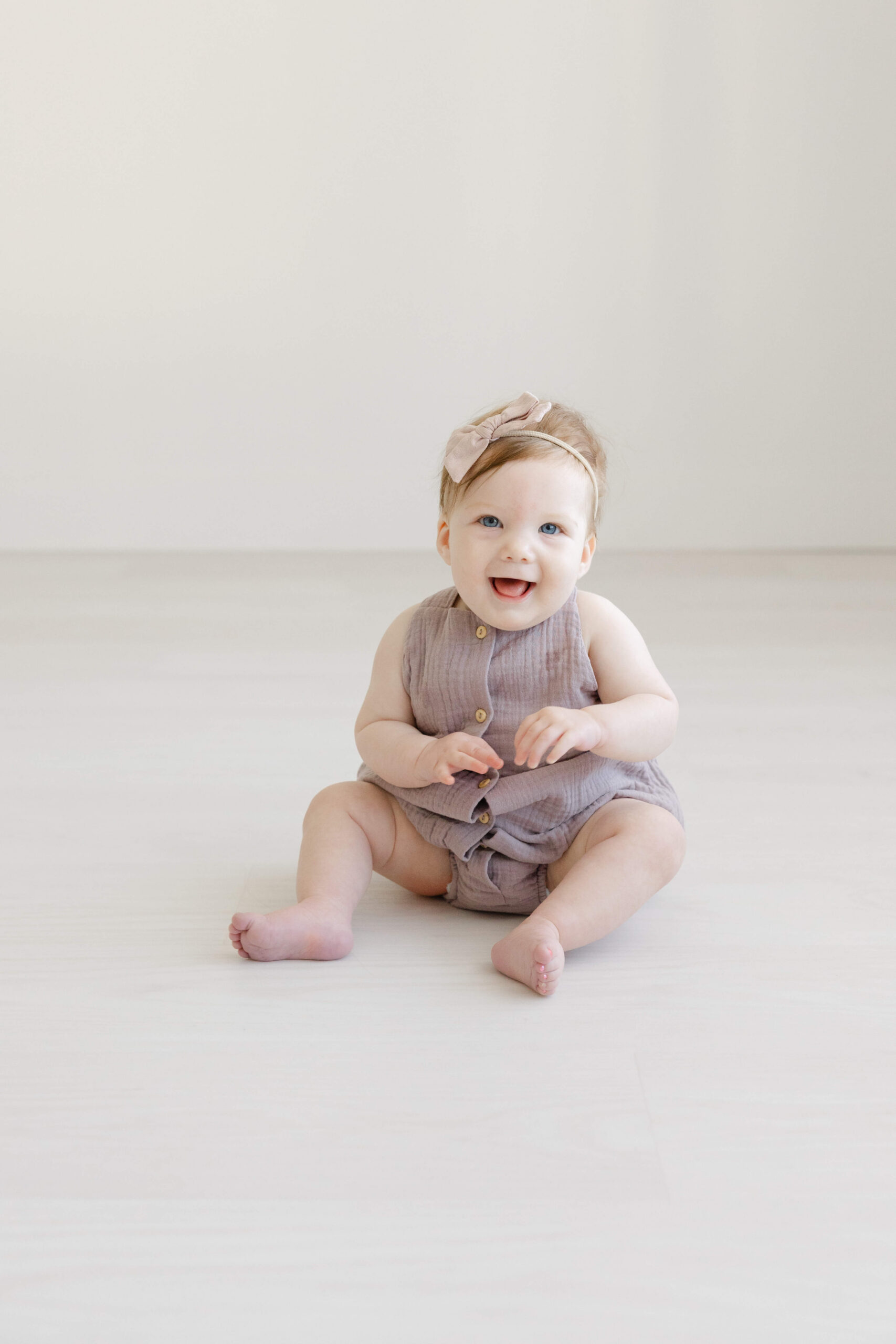 A giggling girl in a purple onesie sits on the floor of a studio after some baby music classes in jacksonville fl