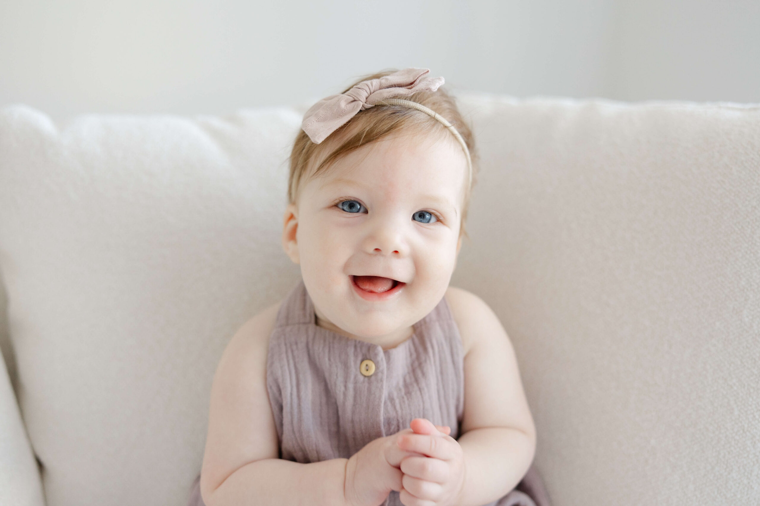 A smiling toddler girl in a purple dress sits on a couch clapping in a close up after some baby music classes in jacksonville fl