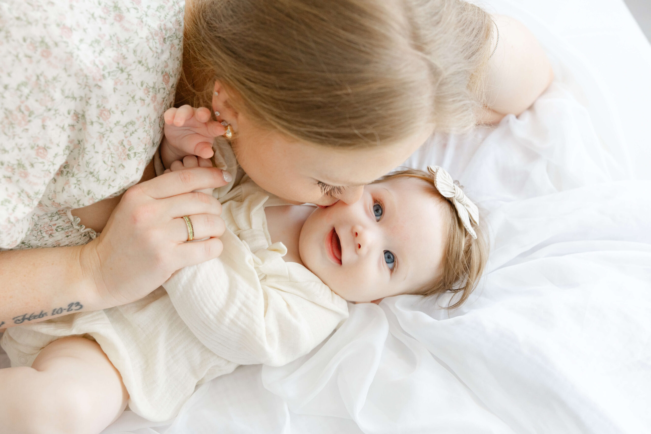 Mom snuggles and kisses her toddler toddler on a bed in a studio after jacksonville library story time