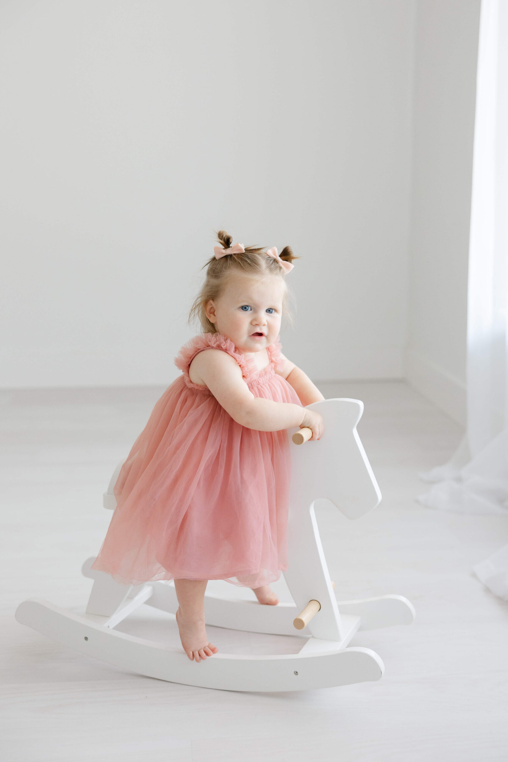 A toddler girl in a pink dress plays on a rocking horse in a window after finding preschools in jacksonville fl