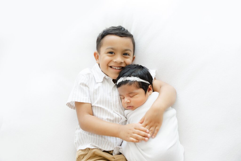 Newborn photographer in Jacksonville featuring sibling hugging new baby